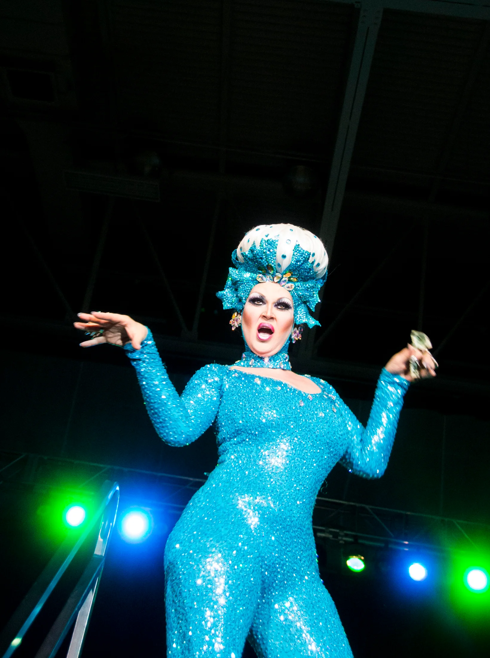 A drag performer in a blue costume photographed from a low angle under stage lights.