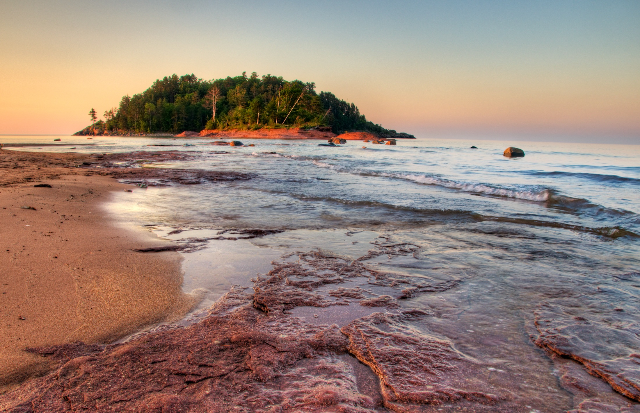Little Presque shoreline at sunset with warm light across the beach, rocks, and water.