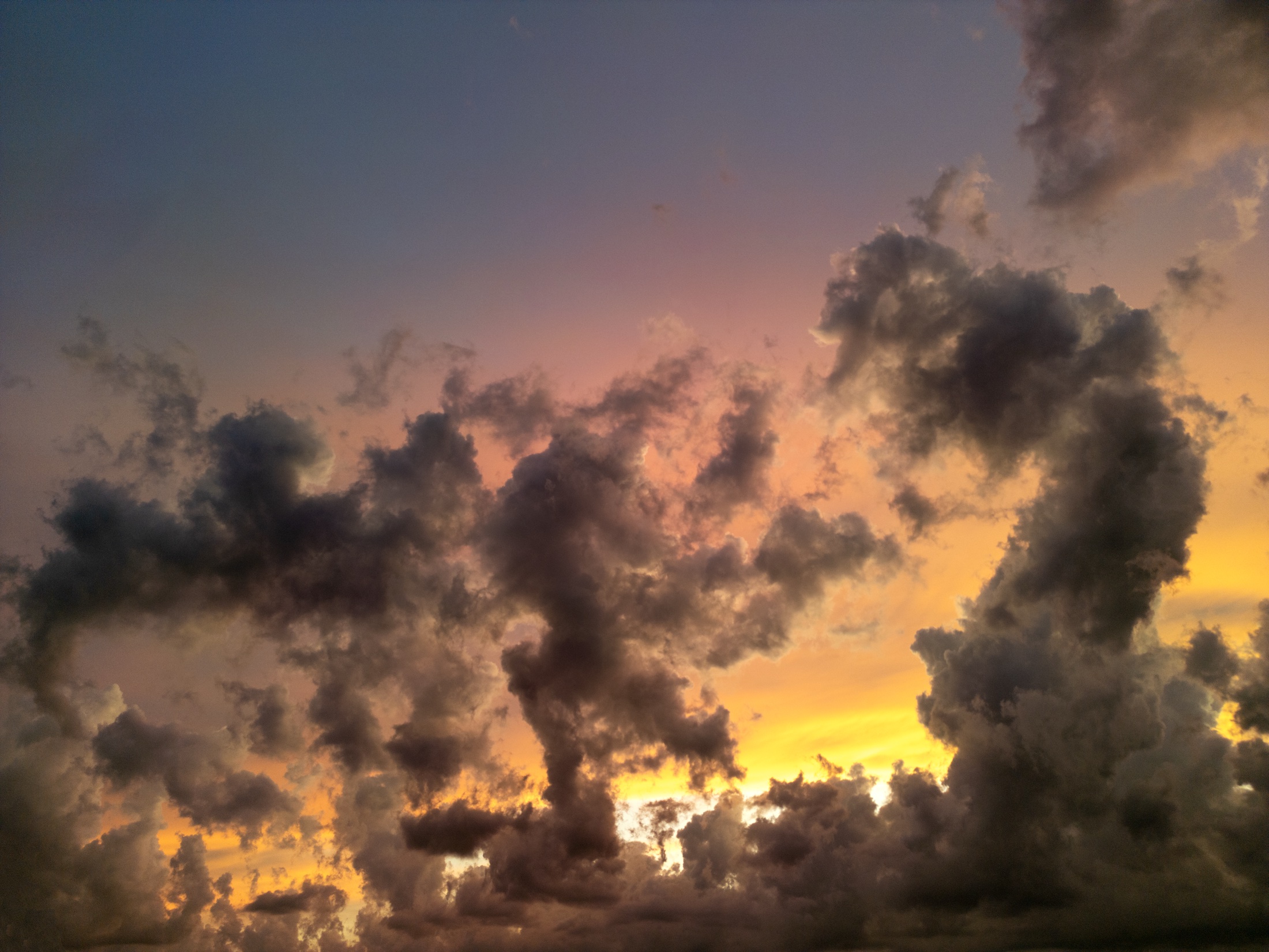 Dark clouds moving across a warm orange and purple sunset sky.