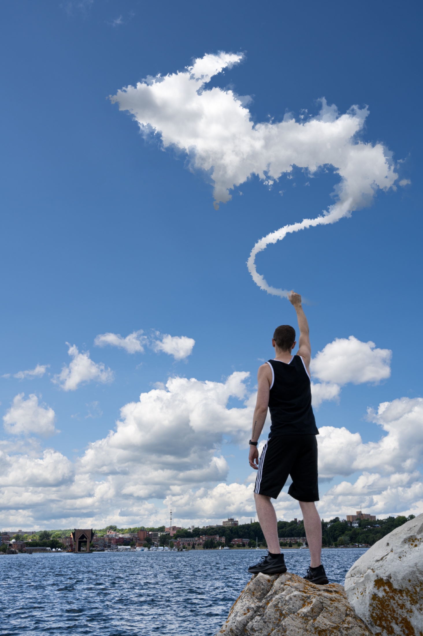 A figure standing on rocks by water, pulling a cloud into a long shape overhead.