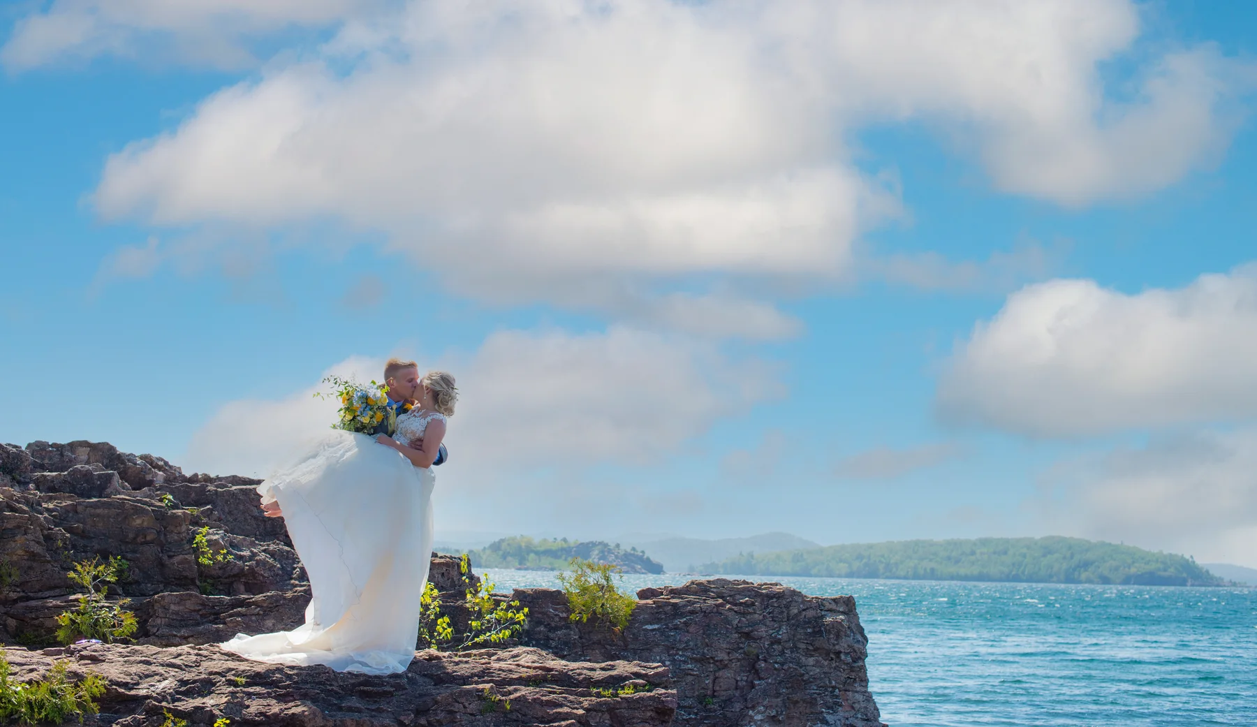 A couple standing on rocky shoreline cliffs with Lake Superior and large clouds behind them.