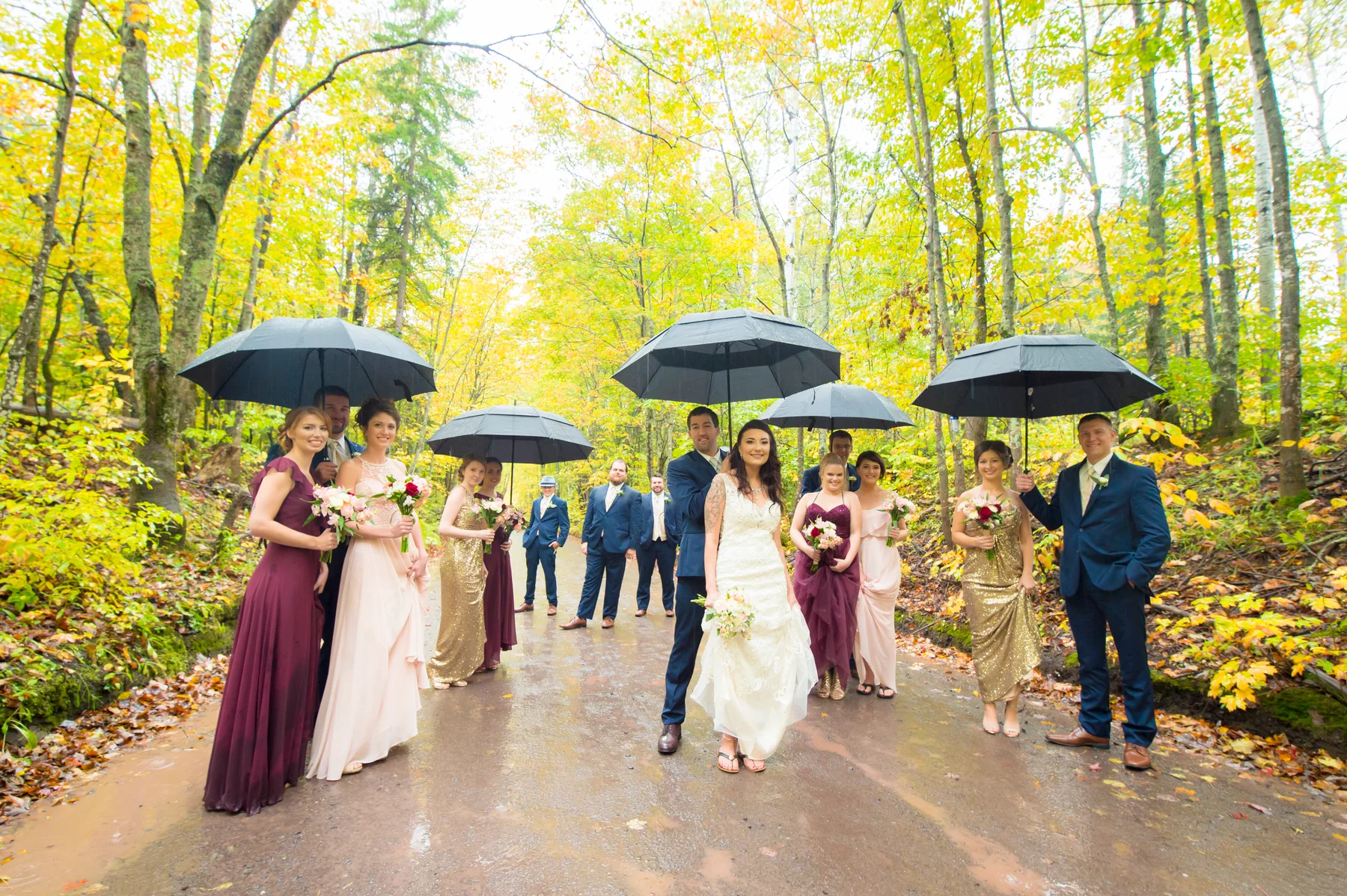 A wedding party standing with umbrellas on a forest road in autumn.