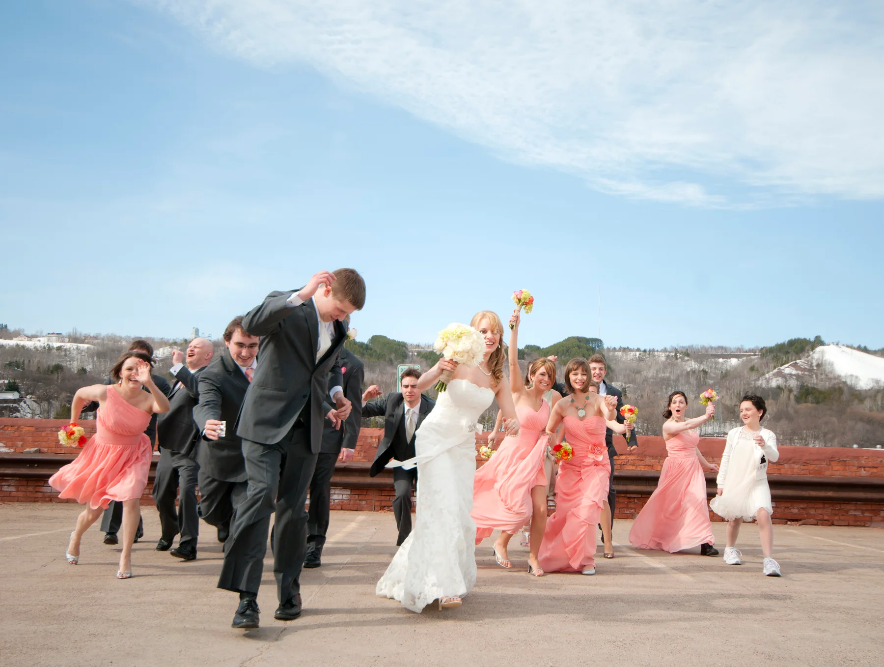 A wedding party running together on a rooftop with hills in the background.