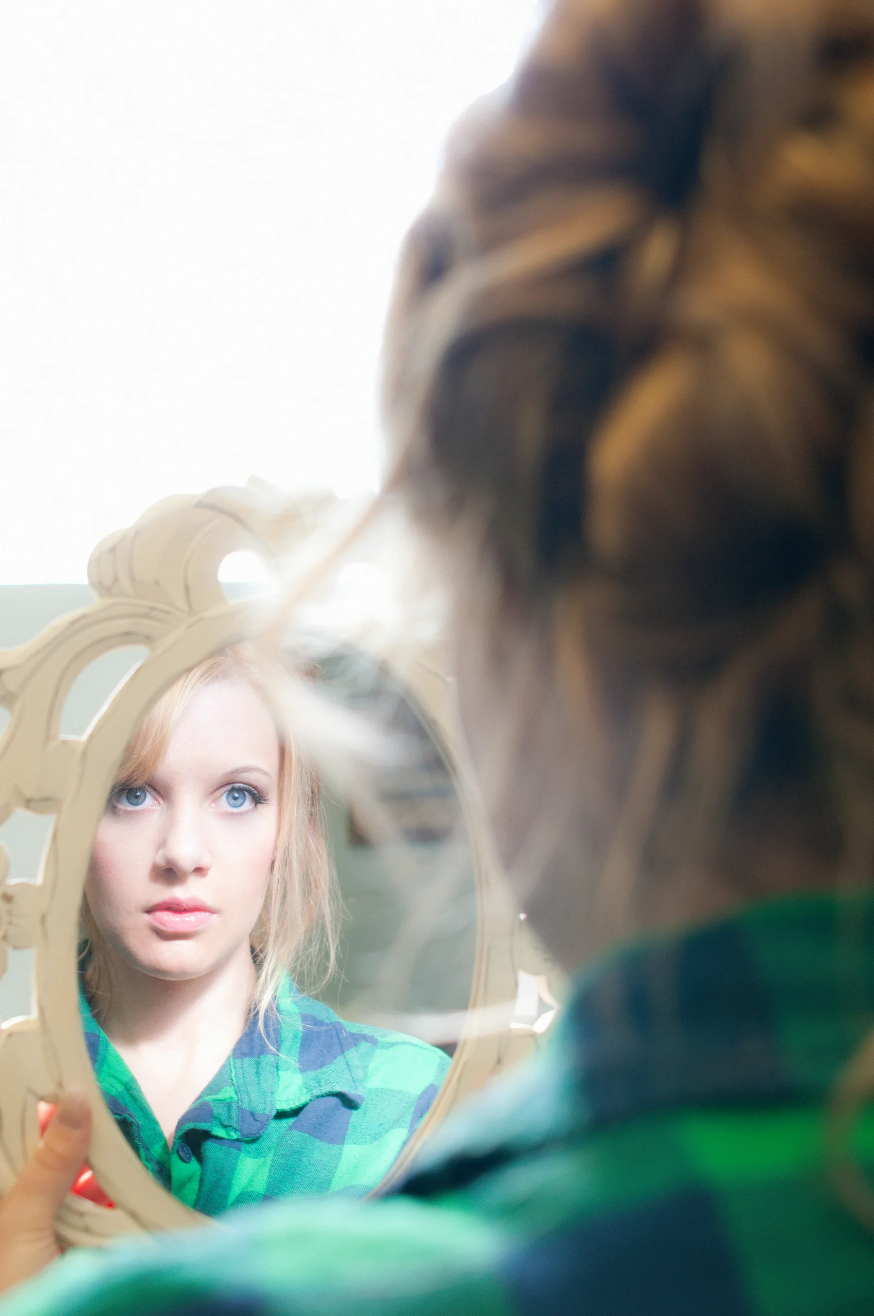 A bride looking into a hand mirror while getting ready.