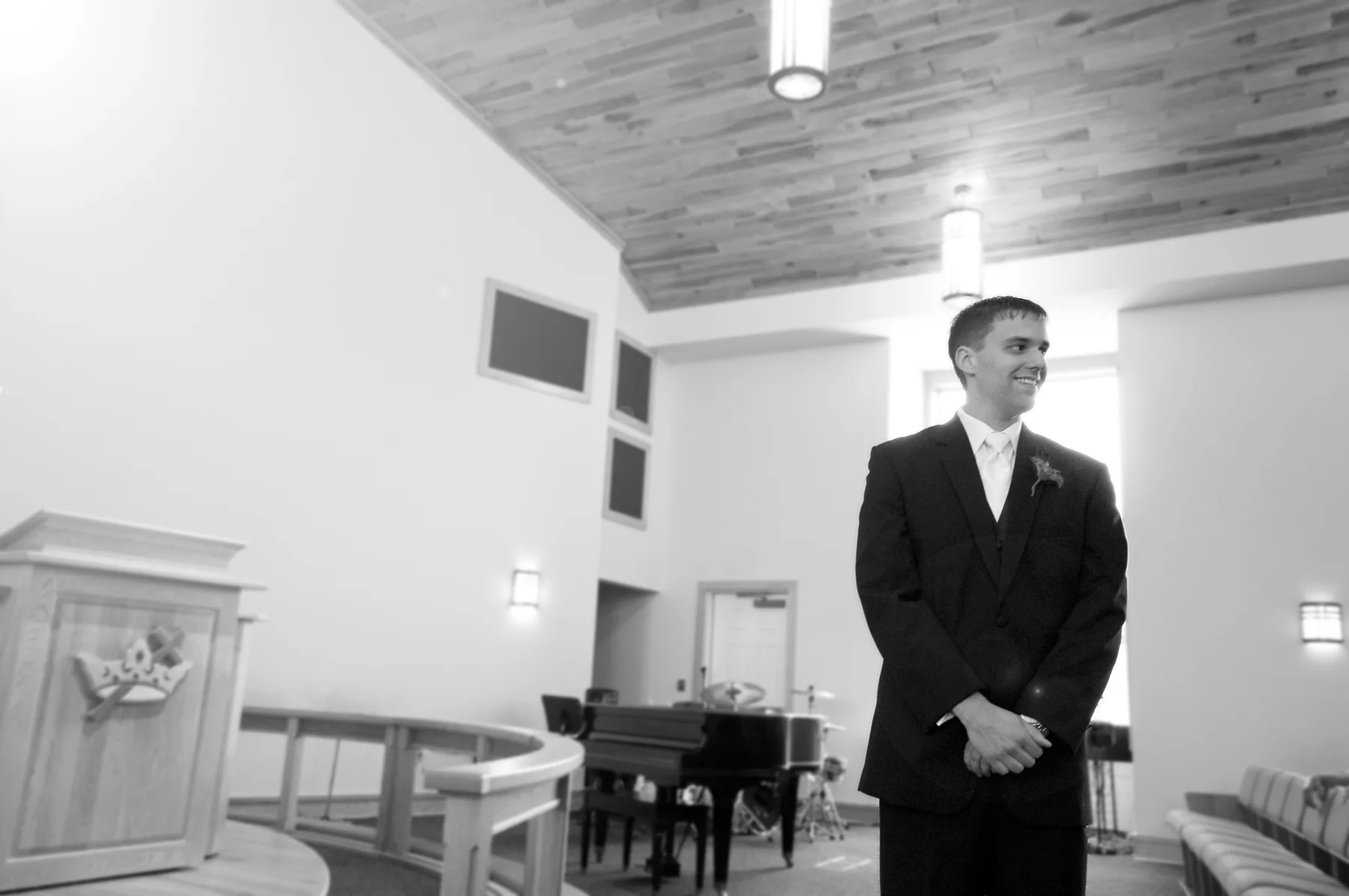 A groom walking outdoors with an officiant between wooden doors and framed family photographs.