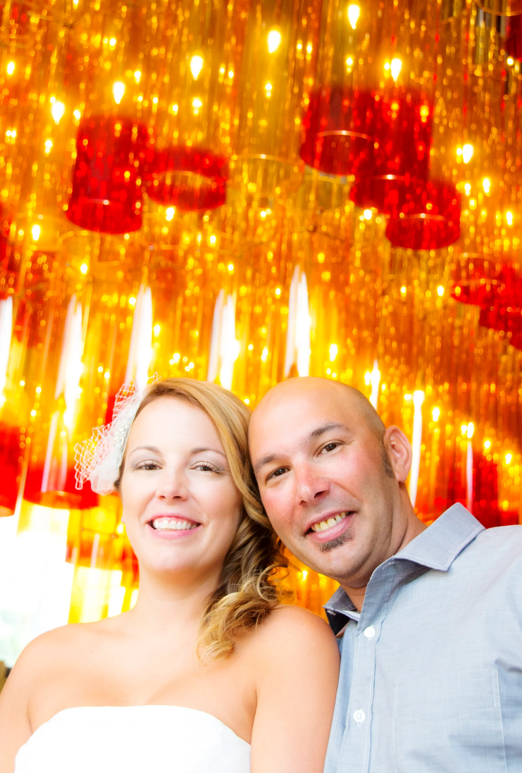 A smiling couple photographed beneath bright red and gold lights.