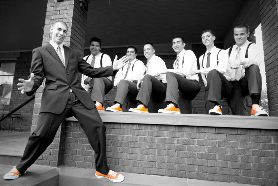 A groom and groomsmen posing in black and white with orange shoes.